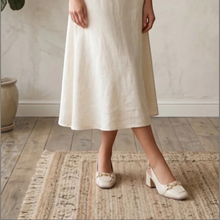 MOODBOARD beige leather slingback pumps with a gold horsebit detail worn by a woman in a cream linen skirt