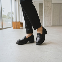 MOODBOARD black synthetic loafers with a chunky sole worn with black trousers in a bright indoor setting