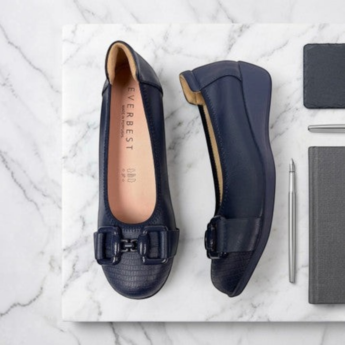 MOODBOARD Everbest navy blue leather wedge pumps with a decorative buckle detail on a marble surface.