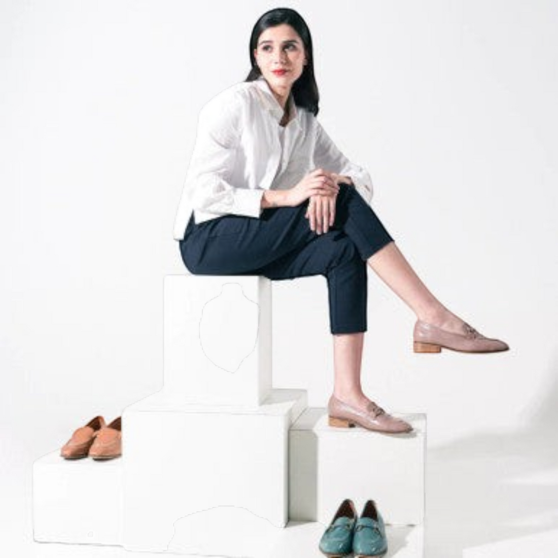 MOODBOARD model wearing beige leather loafers, sitting on white blocks with additional loafers displayed nearby.